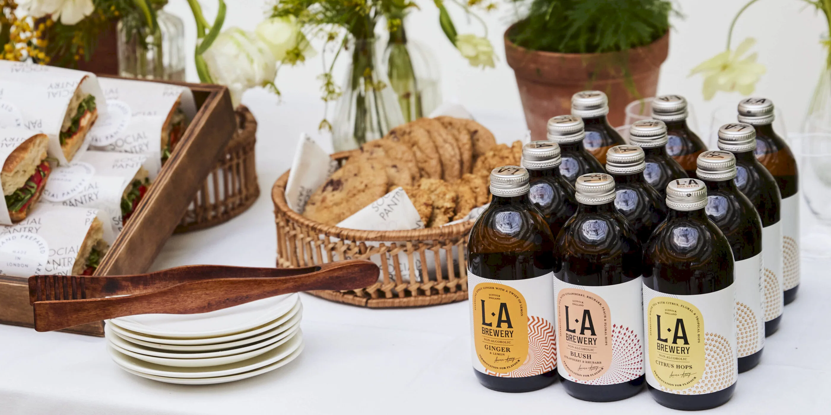 Sandwiches, chocolate chip cookies, bottled soft drinks and yellow flowers on a table